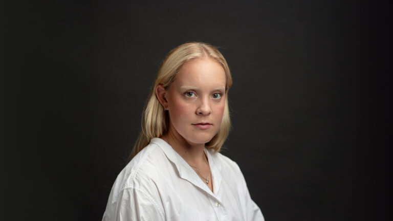 Näyttelijäkuva Emma Pälsynahosta. Emma katsoo kuvassa suoraan kameraan päällään valkoinen paita mustalla taustalla.